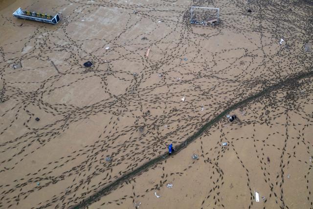 This aerial photograph shows a person walking through footprints in the mud covering a football pitch, two days after flooding caused by what officials said was the heaviest rainfall in the city since records began more than 80 years ago, in the Ayazaga district of Istanbul on October 16, 2026. (Photo by Yasin AKGUL / AFP)