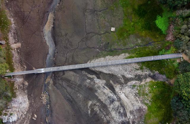 This aerial photograph shows a pedestrian bridge on Lake Drennec, where water levels have dropped due to drought, in Sizun, western France, on October 14, 2026. Water resources in the Brest area and across the Finistère department are under severe pressure due to a significant rainfall deficit. (Photo by Fred TANNEAU / AFP)