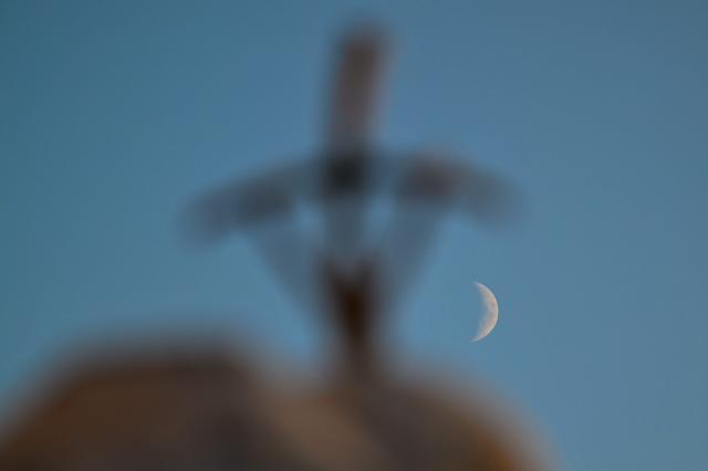 A picture shows the moon behind the statue of John Paul II outside the Gemelli University Hospital, where Pope Leo XIV is recovering after undergoing surgery to remove a cancerous tumour from his right lung, in Rome on October 16, 2026. (Photo by Alberto PIZZOLI / AFP)