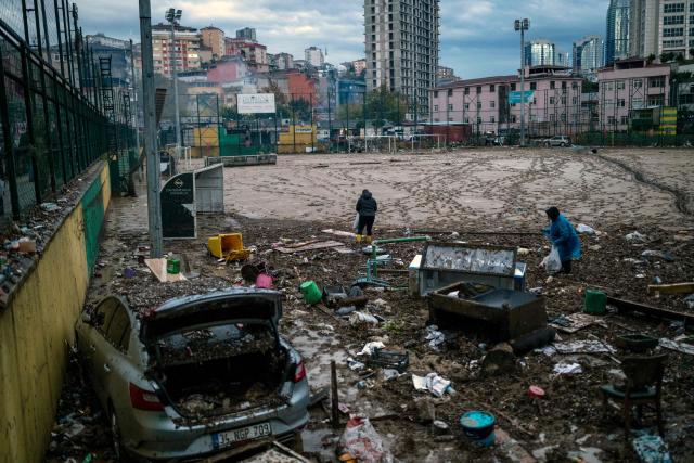 Women work on a football pitch covered with mud, near a wrecked car one day after heavy rain caused flooding in the Ayazaga district of Istanbul on October 16, 2026. Istanbul was on October 15, 2026 battling to recover from flooding caused by what officials said was the heaviest rainfall in the city since records began more than 80 years ago, as the downpour continued. The rain began lashing Turkey's largest city in earnest on Wednesday morning and intensified throughout the day, causing chaos and flash flooding, with footage showing cars being dragged away by the fast-flowing waters. (Photo by YASIN AKGUL / AFP)