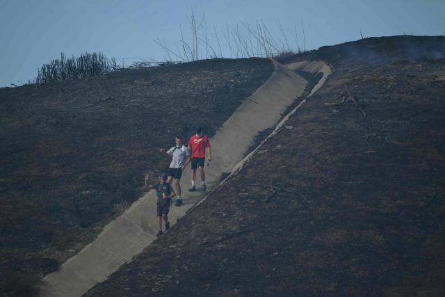 Residents hike through a burn scar above a neighborhood where homes burned during the Norte Fire in San Juan Capistrano, California, on October 16, 2026. Evacuation orders have been issued for parts of Orange County. (Photo by Patrick T. Fallon / AFP)