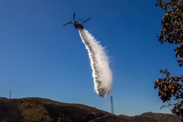 A firefighting helicopter drops water on a hillside at the Bryson Fire in Malibu, California on October 16, 2026. A brush fire in the mountains west of Los Angeles prompted evacuation warnings from officials on Thursday, as powerful winds risked spreading the blaze rapidly. (Photo by Apu GOMES / AFP)