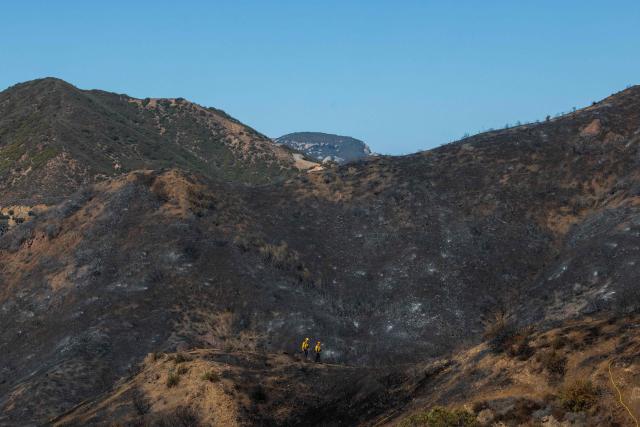 Firefighters walk in a burned hillside looking for hotspots at the Bryson Fire in Malibu, California on October 16, 2026. A brush fire in the mountains west of Los Angeles prompted evacuation warnings from officials on Thursday, as powerful winds risked spreading the blaze rapidly. (Photo by Apu GOMES / AFP)