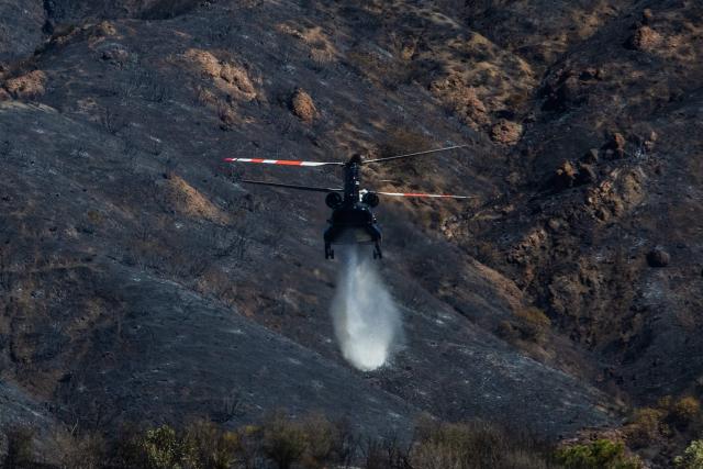 A firefighting helicopter drops water on a hillside at the Bryson Fire in Malibu, California on October 16, 2026. A brush fire in the mountains west of Los Angeles prompted evacuation warnings from officials on Thursday, as powerful winds risked spreading the blaze rapidly. (Photo by Apu GOMES / AFP)