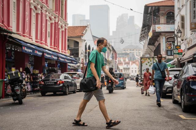 A man wearing a face mask crosses a street in Singapore's Chinatown on October 17, 2026, as the country continues to be shrouded in haze caused by fires in Indonesia. Ongoing fires in Indonesia that have blanketed parts of Southeast Asia with toxic haze have triggered the highest-level alert by the regional bloc's climate and fire monitor. (Photo by Yuichi YAMAZAKI / AFP)
