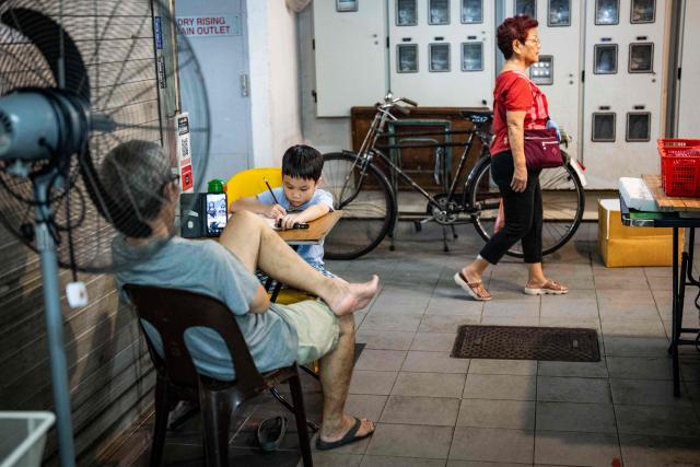 A child (L) studies in a corner of a fresh food market in Singapore's Chinatown on October 17, 2026, as the country continues to be shrouded in haze caused by fires in Indonesia. Ongoing fires in Indonesia that have blanketed parts of Southeast Asia with toxic haze have triggered the highest-level alert by the regional bloc's climate and fire monitor. (Photo by Yuichi YAMAZAKI / AFP)