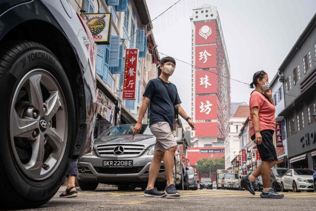 People wearing face masks cross a street in Singapore's Chinatown on October 17, 2026, as the country continues to be shrouded in haze caused by fires in Indonesia. Ongoing fires in Indonesia that have blanketed parts of Southeast Asia with toxic haze have triggered the highest-level alert by the regional bloc's climate and fire monitor. (Photo by Yuichi YAMAZAKI / AFP)