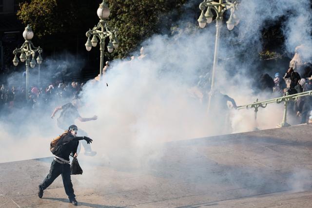 Protesters throws stones among tear gas during clashes on the stairs of Marseille Saint Charles train station prior to the start of a demonstration to protest against the "high cost of living", in Marseille, southern France, on October 17, 2026 as part of a nationwide call for mobilisation bringing together various groups expressing their anger: former "Yellow Vests", secondary school and university students, climate activists and even farmers. After weeks of student protests, France faces broader, nationwide demonstrations on October 17, 2026 over the cost of living, setting up a potentially fraught six months heading into a presidential election. A police source told AFP that authorities estimated nearly 200,000 people could take part, with 40,000 in Paris. (Photo by Thibaud MORITZ / AFP)
