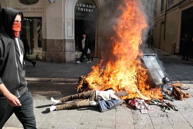 A protesters walks past a pile of burnt objects, including mannequins from a nearby clothing store, prior to the start of a demonstration to protest against the "high cost of living", in Marseille, southern France, on October 17, 2026 as part of a nationwide call for mobilisation bringing together various groups expressing their anger: former "Yellow Vests", secondary school and university students, climate activists and even farmers. After weeks of student protests, France faces broader, nationwide demonstrations on October 17, 2026 over the cost of living, setting up a potentially fraught six months heading into a presidential election. A police source told AFP that authorities estimated nearly 200,000 people could take part, with 40,000 in Paris. (Photo by Thibaud MORITZ / AFP)