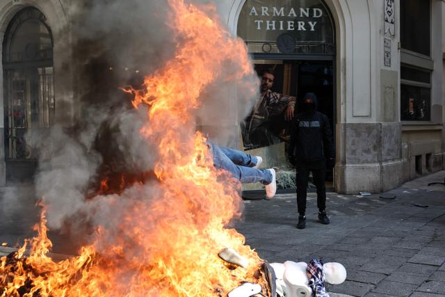A protester stands in front of a pile of burnt objects, including mannequins from a nearby clothing store, prior to the start of a demonstration to protest against the "high cost of living", in Marseille, southern France, on October 17, 2026 as part of a nationwide call for mobilisation bringing together various groups expressing their anger: former "Yellow Vests", secondary school and university students, climate activists and even farmers. After weeks of student protests, France faces broader, nationwide demonstrations on October 17, 2026 over the cost of living, setting up a potentially fraught six months heading into a presidential election. A police source told AFP that authorities estimated nearly 200,000 people could take part, with 40,000 in Paris. (Photo by Thibaud MORITZ / AFP)