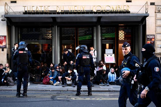 Riot police watch as youth sit in front of the Vieux Colombier theatre ahead of a demonstration to protest against the "high cost of living", in Paris on October 17, 2026 as part of a nationwide call for mobilisation bringing together various groups expressing their anger: former "Yellow Vests", secondary school and university students, climate activists and even farmers. After weeks of student protests, France faces broader, nationwide demonstrations on October 17, 2026 over the cost of living, setting up a potentially fraught six months heading into a presidential election. A police source told AFP that authorities estimated nearly 200,000 people could take part, with 40,000 in Paris. (Photo by Guillaume Saligot / AFP)