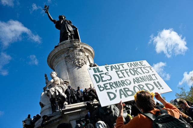 A protester holds a placard reading "shall we make efforts? Bernard Arnault first!" ahead of a demonstration to protest against the "high cost of living", at Place de la Republique in Paris on October 17, 2026 as part of a nationwide call for mobilisation bringing together various groups expressing their anger: former "Yellow Vests", secondary school and university students, climate activists and even farmers. After weeks of student protests, France faces broader, nationwide demonstrations on October 17, 2026 over the cost of living, setting up a potentially fraught six months heading into a presidential election. A police source told AFP that authorities estimated nearly 200,000 people could take part, with 40,000 in Paris. (Photo by Matthieu RONDEL / AFP)