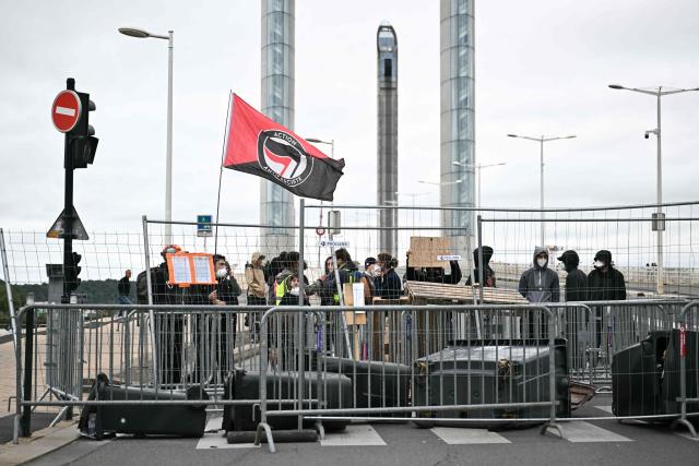 A protester waves a flag of the 'Action Antifasciste' during a  blockage of the Jacques Chaban-Delmas bridge to protest against the "high cost of living"  in Bordeaux, southwestern France, on October 17, 2026 as part of a nationwide call for mobilisation bringing together various groups expressing their anger: former "Yellow Vests", secondary school and university students, climate activists and even farmers. After weeks of student protests, France faces broader, nationwide demonstrations on October 17, 2026 over the cost of living, setting up a potentially fraught six months heading into a presidential election. A police source told AFP that authorities estimated nearly 200,000 people could take part, with 40,000 in Paris. (Photo by Christophe ARCHAMBAULT / AFP)