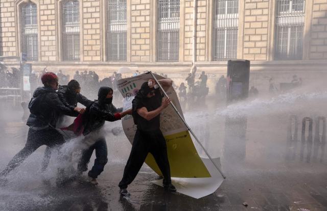 Protesters shield themselves from police water cannons during a demonstration to protest against the "high cost of living", at Place de la Republique in Paris on October 17, 2026 as part of a nationwide call for mobilisation bringing together various groups expressing their anger: former "Yellow Vests", secondary school and university students, climate activists and even farmers. After weeks of student protests, France faces broader, nationwide demonstrations on October 17, 2026 over the cost of living, setting up a potentially fraught six months heading into a presidential election. A police source told AFP that authorities estimated nearly 200,000 people could take part, with 40,000 in Paris. (Photo by Kiran RIDLEY / AFP)
