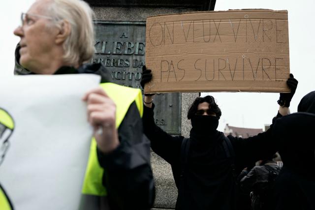 A protester holds a placard reading "We want to live not just survive" during a demonstration against the "high cost of living", in Strasbourg, northeastern France, on October 17, 2026 as part of a nationwide call for mobilisation bringing together various groups expressing their anger: former "Yellow Vests", secondary school and university students, climate activists and even farmers. After weeks of student protests, France faces broader, nationwide demonstrations on October 17, 2026 over the cost of living, setting up a potentially fraught six months heading into a presidential election. A police source told AFP that authorities estimated nearly 200,000 people could take part, with 40,000 in Paris. (Photo by ROMEO BOETZLE / AFP)
