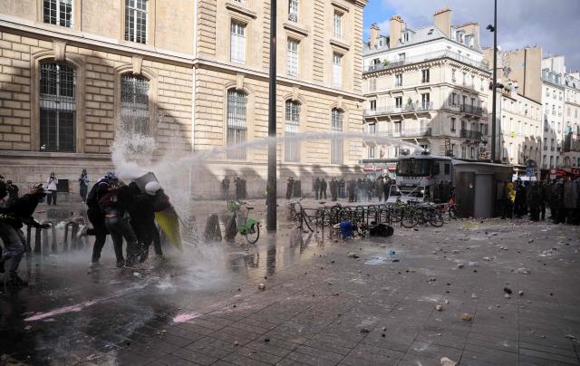Protesters shield themselves from police water cannons during a demonstration to protest against the "high cost of living", at Place de la Republique in Paris on October 17, 2026 as part of a nationwide call for mobilisation bringing together various groups expressing their anger: former "Yellow Vests", secondary school and university students, climate activists and even farmers. After weeks of student protests, France faces broader, nationwide demonstrations on October 17, 2026 over the cost of living, setting up a potentially fraught six months heading into a presidential election. A police source told AFP that authorities estimated nearly 200,000 people could take part, with 40,000 in Paris. (Photo by Kiran RIDLEY / AFP)