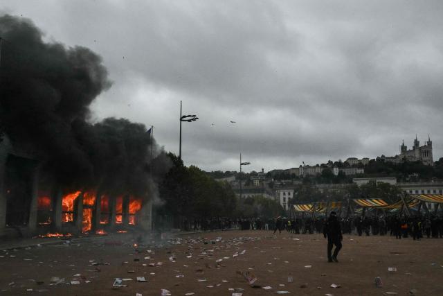 Protesters stand by Lyon's tourism office set on fire during a demonstration to protest against the "high cost of living", in Lyon, southeastern France, on October 17, 2026 as part of a nationwide call for mobilisation bringing together various groups expressing their anger: former "Yellow Vests", secondary school and university students, climate activists and even farmers. After weeks of student protests, France faces broader, nationwide demonstrations on October 17, 2026 over the cost of living, setting up a potentially fraught six months heading into a presidential election. A police source told AFP that authorities estimated nearly 200,000 people could take part, with 40,000 in Paris. (Photo by Jeff PACHOUD / AFP)