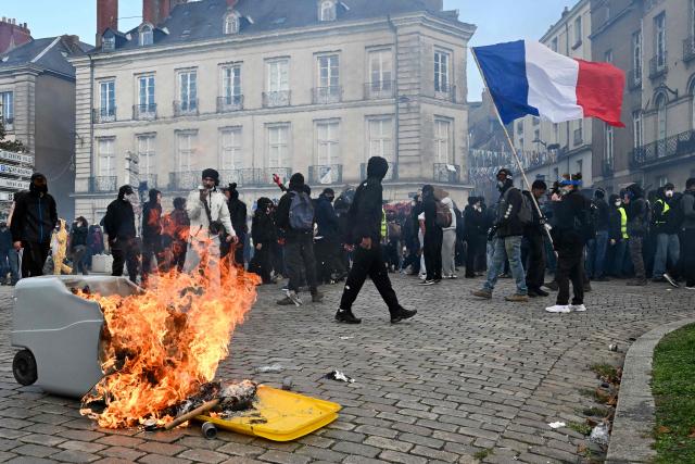 A protester waves a French flag next to a trash can fire during a demonstration to protest against the "high cost of living", in Nantes, western France, on October 17, 2026 as part of a nationwide call for mobilisation bringing together various groups expressing their anger: former "Yellow Vests", secondary school and university students, climate activists and even farmers. After weeks of student protests, France faces broader, nationwide demonstrations on October 17, 2026 over the cost of living, setting up a potentially fraught six months heading into a presidential election. A police source told AFP that authorities estimated nearly 200,000 people could take part, with 40,000 in Paris. (Photo by Sebastien Salom-Gomis / AFP)