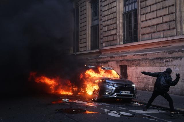 A protester throws a projectile while standing in front of a car on fire during a demonstration to protest against the "high cost of living", in Paris on October 17, 2026 as part of a nationwide call for mobilisation bringing together various groups expressing their anger: former "Yellow Vests", secondary school and university students, climate activists and even farmers. After weeks of student protests, France faces broader, nationwide demonstrations on October 17, 2026 over the cost of living, setting up a potentially fraught six months heading into a presidential election. A police source told AFP that authorities estimated nearly 200,000 people could take part, with 40,000 in Paris. (Photo by Kiran RIDLEY / AFP)