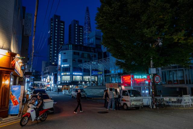 People gather in front of a food truck (R) as the landmark Lotte World Tower (back) is seen from an inner street in the Songpa district of Seoul on October 17, 2026. (Photo by Philip FONG / AFP)