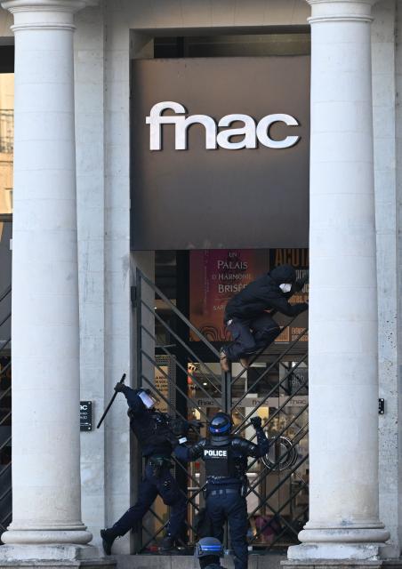 French police officers confront a protester climbing the fence of a fnac store during a demonstration against the "high cost of living", in Nantes, western France, on October 17, 2026 as part of a nationwide call for mobilisation bringing together various groups expressing their anger: former "Yellow Vest", secondary school and university students, climate activists and even farmers. After weeks of student protests, France faces broader, nationwide demonstrations on October 17, 2026 over the cost of living, setting up a potentially fraught six months heading into a presidential election. A police source told AFP that authorities estimated nearly 200,000 people could take part, with 40,000 in Paris. (Photo by Sebastien Salom-Gomis / AFP)
