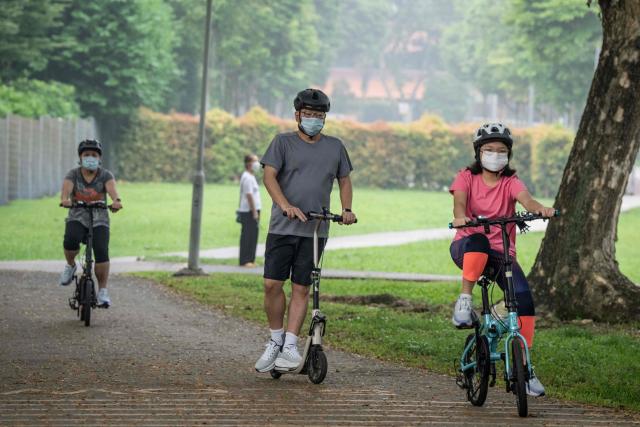 People wearing face masks ride bicycles and scooters through a park in Singapore on October 18, 2026, as the country continues to be shrouded in haze caused by fires in Indonesia. Ongoing fires in Indonesia that have blanketed parts of Southeast Asia with toxic haze have triggered the highest-level alert by the regional bloc's climate and fire monitor. (Photo by Yuichi YAMAZAKI / AFP)