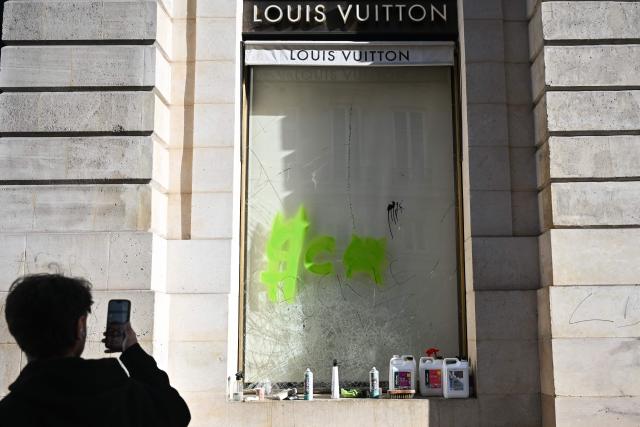 A pedestrian takes pictures of the damaged "Louis Vuitton" shop, in central Paris on October 18, 2026, a day after nationwide protests against the "high cost of living". France's Prime Minister Sebastien Lecornu said 1,200 people were arrested in protests across the country on October 17, and 150 police were hurt as Clashes between police and protesters, massive looting and multiple blazes gripped France as nationwide marches against soaring inflation degenerated into street violence of "extreme intensity". (Photo by Matthieu RONDEL / AFP)