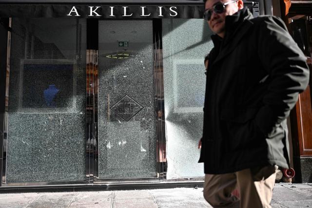 A pedestrian walks past a damaged front window of a shop, in central Paris on October 18, 2026, a day after nationwide protests against the "high cost of living". France's Prime Minister Sebastien Lecornu said 1,200 people were arrested in protests across the country on October 17, and 150 police were hurt as Clashes between police and protesters, massive looting and multiple blazes gripped France as nationwide marches against soaring inflation degenerated into street violence of "extreme intensity". (Photo by Matthieu RONDEL / AFP)