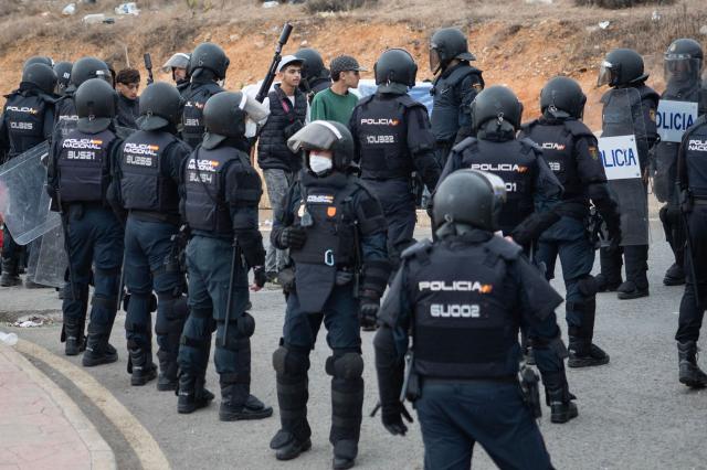 Spanish police escort migrants onto buses after rounding up migrants sleeping rough outside the Tarajal warehouses on the outskirts of Spain's north African enclave of Ceuta on October 18, 2026. Scores of migrants remain sleeping rough in outlying neighborhoods of the city since the massive influx of tens of thousands of migrants from Morocco in late July, fueling tension in this Spanish North African enclave of some 80,000 inhabitants. Migrants are being transported by bus to police facilities, with minors taken to the National Police headquarters and adults transferred to the Tarajal Temporary Assistance Centre for Foreigners (CATE) for identification, registration and screening. (Photo by Antonio Sempere / AFP)