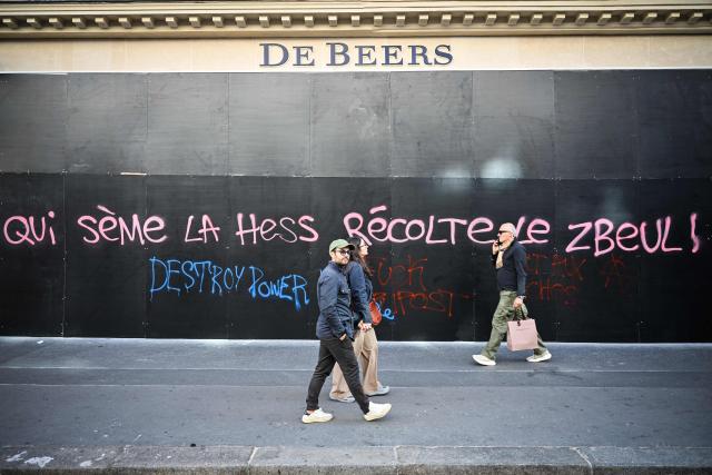 Pedestrians walk past a tag reading "Whoever sows hardship reaps chaos" on the frontage of the jewellery shop "De Beers" in central Paris, on October 18, 2026 a day after nationwide protests against the "high cost of living". France's Prime Minister Sebastien Lecornu said 1,200 people were arrested in protests across the country on October 17, and 150 police were hurt as Clashes between police and protesters, massive looting and multiple blazes gripped France as nationwide marches against soaring inflation degenerated into street violence of "extreme intensity". (Photo by Matthieu RONDEL / AFP)