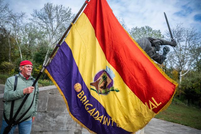 A demonstrator holds an International Brigade flag at a Berlin memorial for German members of the International Brigades who fought for Republican Spain during the Spanish Civil War (1936-39), during a commemoration on the 90th anniversary of the start of the war, and the formation of the International Brigades, on October 18, 2026. Some 4,000 to 5,000 German volunteers, many of them anti-fascist exiles, communists, and working-class veterans of the Weimar Republic, fought in Spain. (Photo by John MACDOUGALL / AFP)