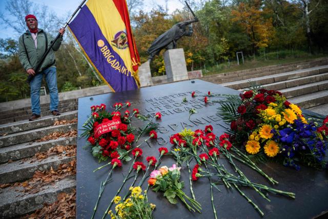 A demonstrator holds an International Brigade flag at a Berlin memorial for German members of the International Brigades who fought for Republican Spain during the Spanish Civil War (1936-39), during a commemoration on the 90th anniversary of the start of the war, and the formation of the International Brigades, on October 18, 2026. Some 4,000 to 5,000 German volunteers, many of them anti-fascist exiles, communists, and working-class veterans of the Weimar Republic, fought in Spain. (Photo by John MACDOUGALL / AFP)