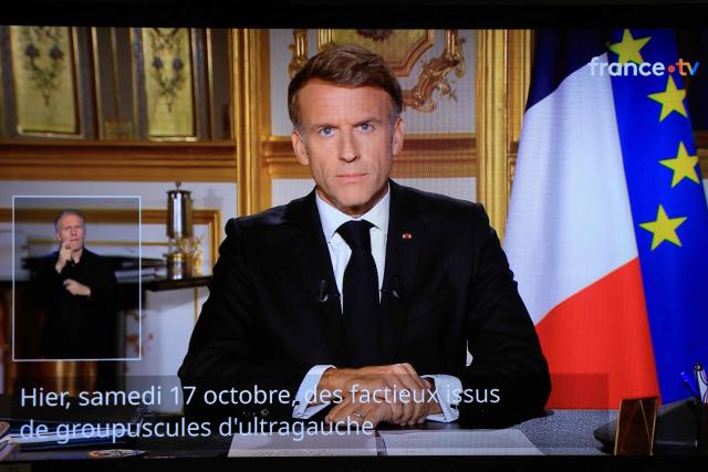 This photograph shows a television monitor broadcasting France's President Emmanuel Macron giving a speech from the Elysee Presidential Palace the day after riots and looting on the sidelines of nationwide protests against the "high cost of living", in Paris on October 18, 2026. France's Interior Minister said 1,800 people were arrested in protests across the country on October 17, and 600 police officers, gendarmes and firefighters were hurt during clashes. On October 17, 550,000 people took part in demonstrations against the high cost of living, including 110,000 in Paris, according to official figures. In many cities across France, the day of protests descended into chaos, marked by clashes and looting. (Photo by Ludovic MARIN / AFP)