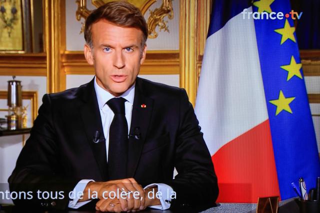 This photograph shows a television monitor broadcasting France's President Emmanuel Macron giving a speech from the Elysee Presidential Palace the day after riots and looting on the sidelines of nationwide protests against the "high cost of living", in Paris on October 18, 2026. France's Interior Minister said 1,800 people were arrested in protests across the country on October 17, and 600 police officers, gendarmes and firefighters were hurt during clashes. On October 17, 550,000 people took part in demonstrations against the high cost of living, including 110,000 in Paris, according to official figures. In many cities across France, the day of protests descended into chaos, marked by clashes and looting. (Photo by Ludovic MARIN / AFP)