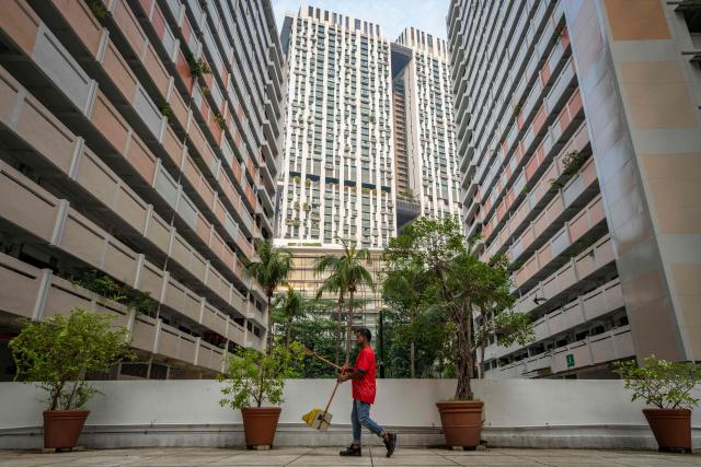 A cleaner walks past public housing apartment blocks in Singapore on October 19, 2026, as the country continues to be shrouded in haze caused by fires in Indonesia. (Photo by Yuichi YAMAZAKI / AFP)