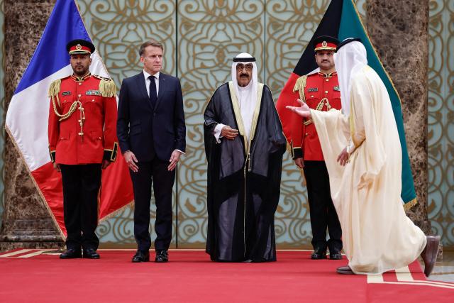 An official gestures the way as French President Emmanuel Macron(2nd L) and the Emir of Kuwait Sheikh Mishal Al-Ahmad Al-Jaber Al-Sabah stand during a welcoming ceremony upon the president's arrival at Kuwait International Airport, in Kuwait City October 19, 2026. (Photo by Benoit Tessier / POOL / AFP)