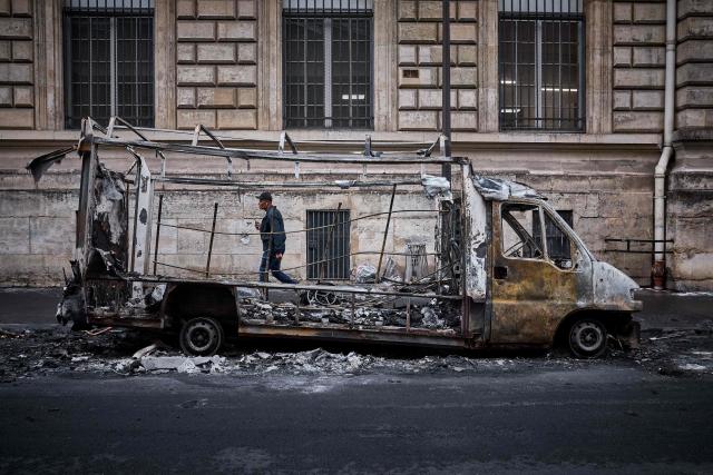 A man walks past a burnt out car on Rue Yves Toudic destroyed after a weekend of protests against the "high cost of living", in central Paris on October 19, 2026. France's Prime Minister said 1,200 people were arrested in protests across the country on October 17, and 150 police were hurt during clashes between police and protesters. Massive looting and multiple blazes gripped France as nationwide marches against soaring inflation degenerated into street violence of "extreme intensity". (Photo by Kiran RIDLEY / AFP)