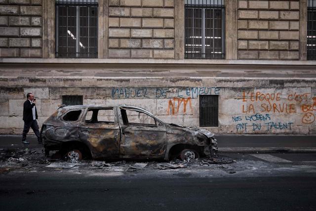 A man walks past a burnt out car on Rue Yves Toudic destroyed after a weekend of protests against the "high cost of living", in central Paris on October 19, 2026. France's Prime Minister said 1,200 people were arrested in protests across the country on October 17, and 150 police were hurt during clashes between police and protesters. Massive looting and multiple blazes gripped France as nationwide marches against soaring inflation degenerated into street violence of "extreme intensity". (Photo by Kiran RIDLEY / AFP)