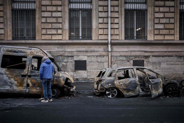 A local resident looks inside a burnt out van on Rue Yves Toudic destroyed after a weekend of protests against the "high cost of living", in central Paris on October 19, 2026. France's Prime Minister said 1,200 people were arrested in protests across the country on October 17, and 150 police were hurt during clashes between police and protesters. Massive looting and multiple blazes gripped France as nationwide marches against soaring inflation degenerated into street violence of "extreme intensity". (Photo by Kiran RIDLEY / AFP)