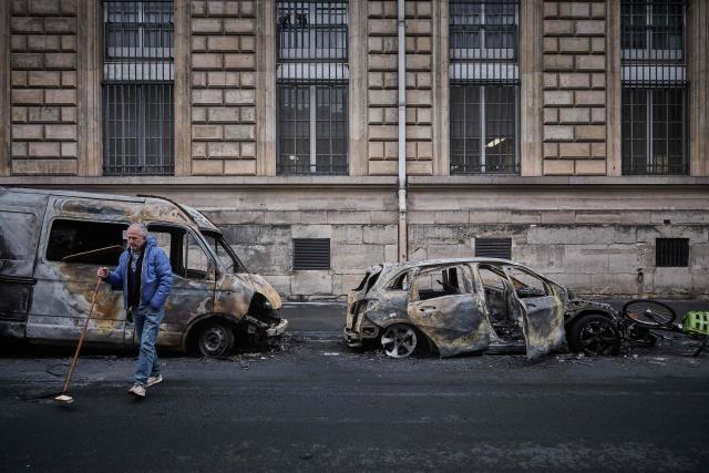 A local resident crosses the street with his broom on Rue Yves Toudic after a weekend of protests against the "high cost of living", in central Paris on October 19, 2026. France's Prime Minister said 1,200 people were arrested in protests across the country on October 17, and 150 police were hurt during clashes between police and protesters. Massive looting and multiple blazes gripped France as nationwide marches against soaring inflation degenerated into street violence of "extreme intensity". (Photo by Kiran RIDLEY / AFP)