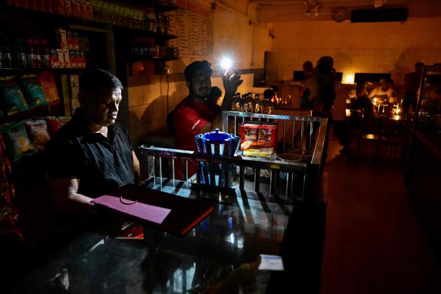 A vendor uses a mobile torchlight at his tea shop in Colombo on October 19, 2026 during a power outage as part of Sri Lanka's electricity rationing measure, two days after a nationwide blackout. Sri Lanka announced nationwide electricity rationing from October 19, two days after a complete breakdown of the national grid caused by a fault at a coal-fired generator. The state-run electricity utility said power would be cut for one hour in stages across the island during a four-hour period from October 19 evening. (Photo by Ishara S. KODIKARA / AFP)