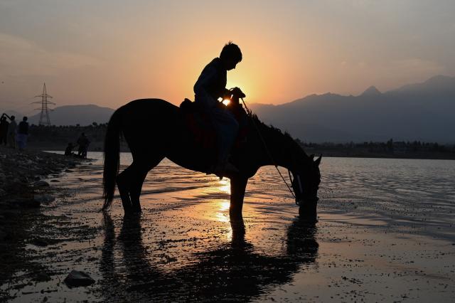 An Afghan boy sits on his horse as it drinks water from the Qargha Lake on the outskirts of Kabul on October 19, 2026. (Photo by Wakil Kohsar / AFP)