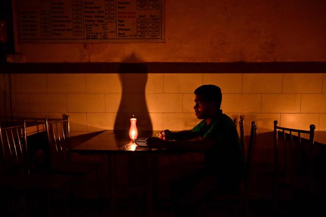 A man uses a candlelight as he drinks tea at a hotel in Colombo on October 19, 2026 during a power outage as part of Sri Lanka's electricity rationing measure, two days after a nationwide blackout. Sri Lanka announced nationwide electricity rationing from October 19, two days after a complete breakdown of the national grid caused by a fault at a coal-fired generator. The state-run electricity utility said power would be cut for one hour in stages across the island during a four-hour period from October 19 evening. (Photo by Ishara S. KODIKARA / AFP)