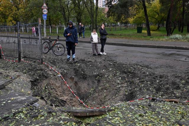 People stand by a missile crater near a school damaged following a Russian ballistic missile attack in Kyiv on October 19, 2026, amid the Russian invasion of Ukraine. (Photo by Sergei SUPINSKY / AFP)