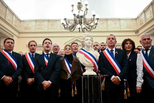 Mayor of Marseille Benoit Payan (3rd L), Mayor of Salon-de-Provence and President of Aix-Marseille Provence Metropole Nicolas Isnard (3rd R), President of the Bouches-du-Rhone Departmental Council Martine Vassal (2nd R) and other invitees sing the French national anthem "La Marseillaise" as they pose next to the new bust of a "Marianne", the symbolic embodiment of France, during a symbolic presentation at the city hall by the Association of French Mayors in Marseille on October 19, 2026. A bust of "Marianne", the symbolic embodiment of France, was damaged on October 17 after dozens of protesters briefly entered the lobby of Marseille's city hall during a nationwide protest against the high cost of living in France. (Photo by Justine MEDDAH / AFP)