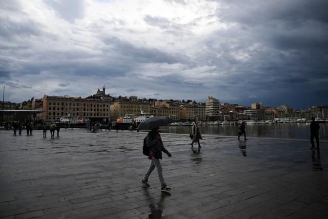 A man walks with an umbrella at Vieux Port in Marseille, southern France, on October 19, 2026. (Photo by Justine Meddah / AFP)
