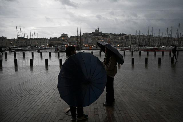 People stand with an umbrellas at Vieux Port in Marseille, southern France, on October 19, 2026. (Photo by Justine Meddah / AFP)