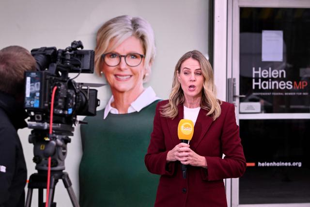 A TV crew works in front of a portrait of Australian politician Helen Haines (C) outside her office in the northern regional city of Wangaratta, about 250 kilometres north-east of Melbourne on October 20, 2026. Australian independent lawmaker Helen Haines underwent surgery overnight but remains in a critical condition after being struck deliberately by a car in an attack, Prime Minister Anthony Albanese said on October 20. Political violence is rare in Australia, but law enforcement have documented a steady rise in threats and abuse directed towards the nation's elected officials in recent years. (Photo by William WEST / AFP)