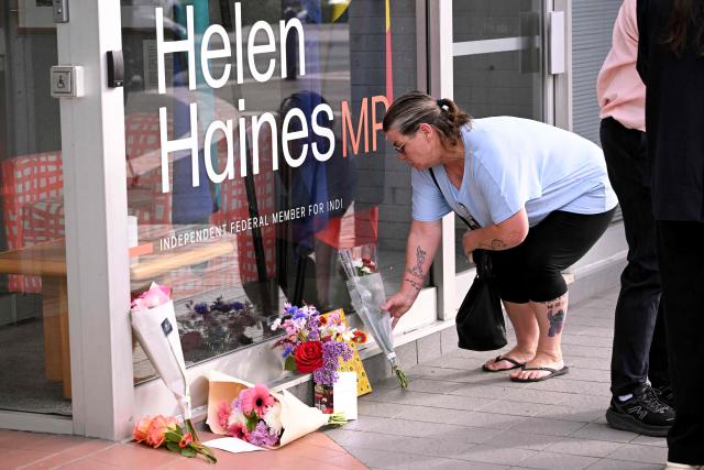 A woman places flowers outside the office of Australian politician Helen Haines in the northern regional city of Wangaratta, about 250 kilometres north-east of Melbourne on October 20, 2026. Australian independent lawmaker Helen Haines underwent surgery overnight but remains in a critical condition after being struck deliberately by a car in an attack, Prime Minister Anthony Albanese said on October 20. Political violence is rare in Australia, but law enforcement have documented a steady rise in threats and abuse directed towards the nation's elected officials in recent years. (Photo by William WEST / AFP)