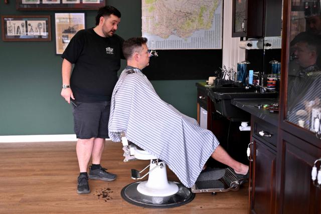 Barber Ricky Jefferies (L) cuts the hair of a customer a day after tackling a man who attacked Australian politician Helen Haines in the northern regional city of Wangaratta about 250 kilometres north-east of Melbourne on October 20, 2026. Australian independent lawmaker Helen Haines underwent surgery overnight but remains in a critical condition after being struck deliberately by a car in an attack, Prime Minister Anthony Albanese said on October 20. Political violence is rare in Australia, but law enforcement have documented a steady rise in threats and abuse directed towards the nation's elected officials in recent years. (Photo by William WEST / AFP)